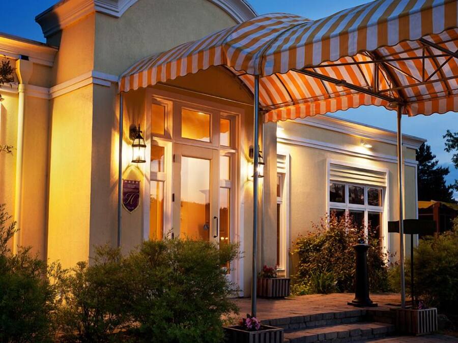 Ingresso di un hotel con portico coperto, facciata ben illuminata e giardino curato.