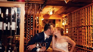 A couple kissing at a bar with wine bottles in the background. - Auberge West Brome (Lac-Brome)