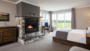 A bedroom with a stone fireplace, a bed, a desk, and a balcony with a view. - Auberge West Brome (Lac-Brome)