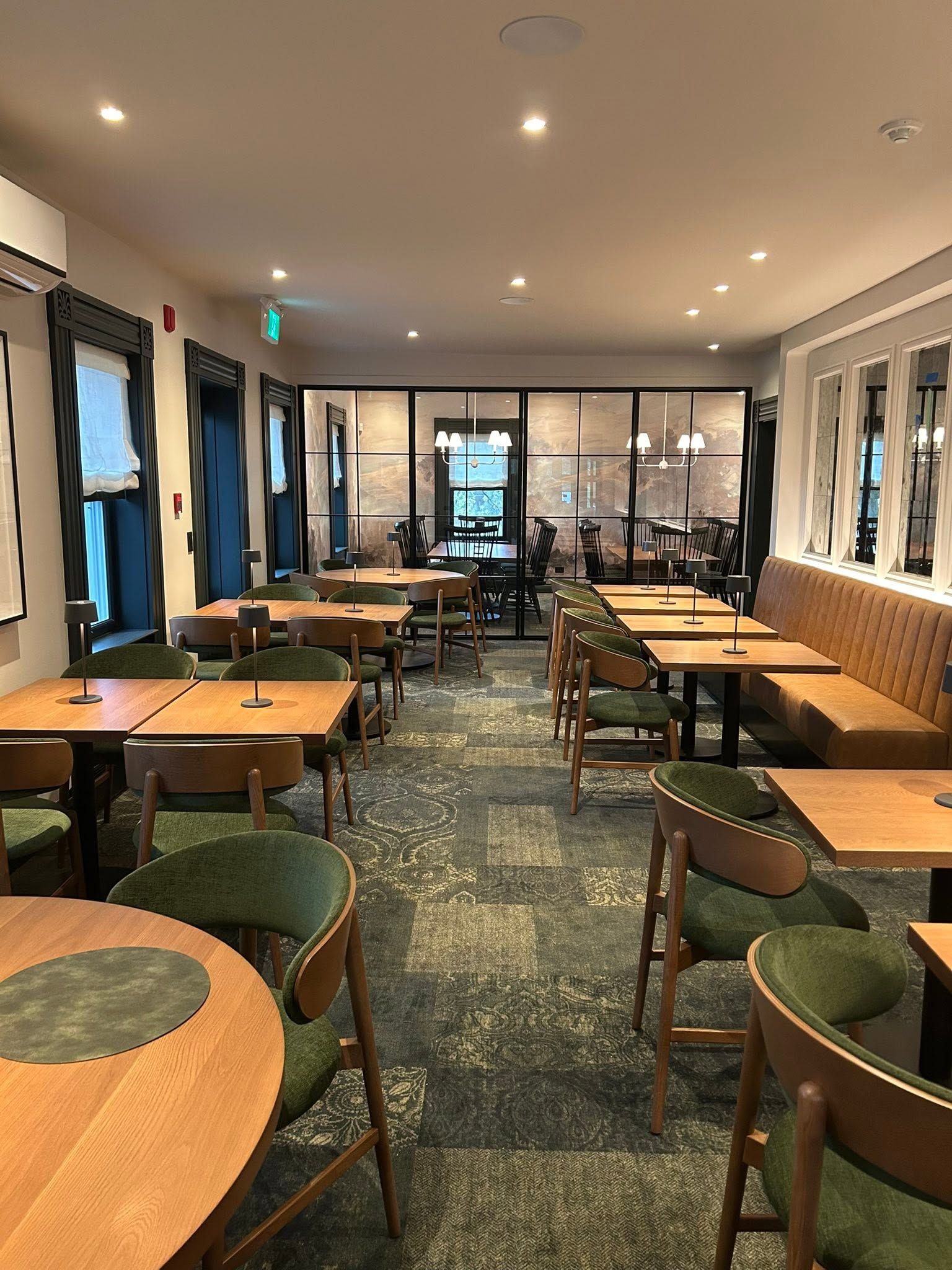 A restaurant with multiple tables and chairs, a patterned carpet, and a view through large windows.