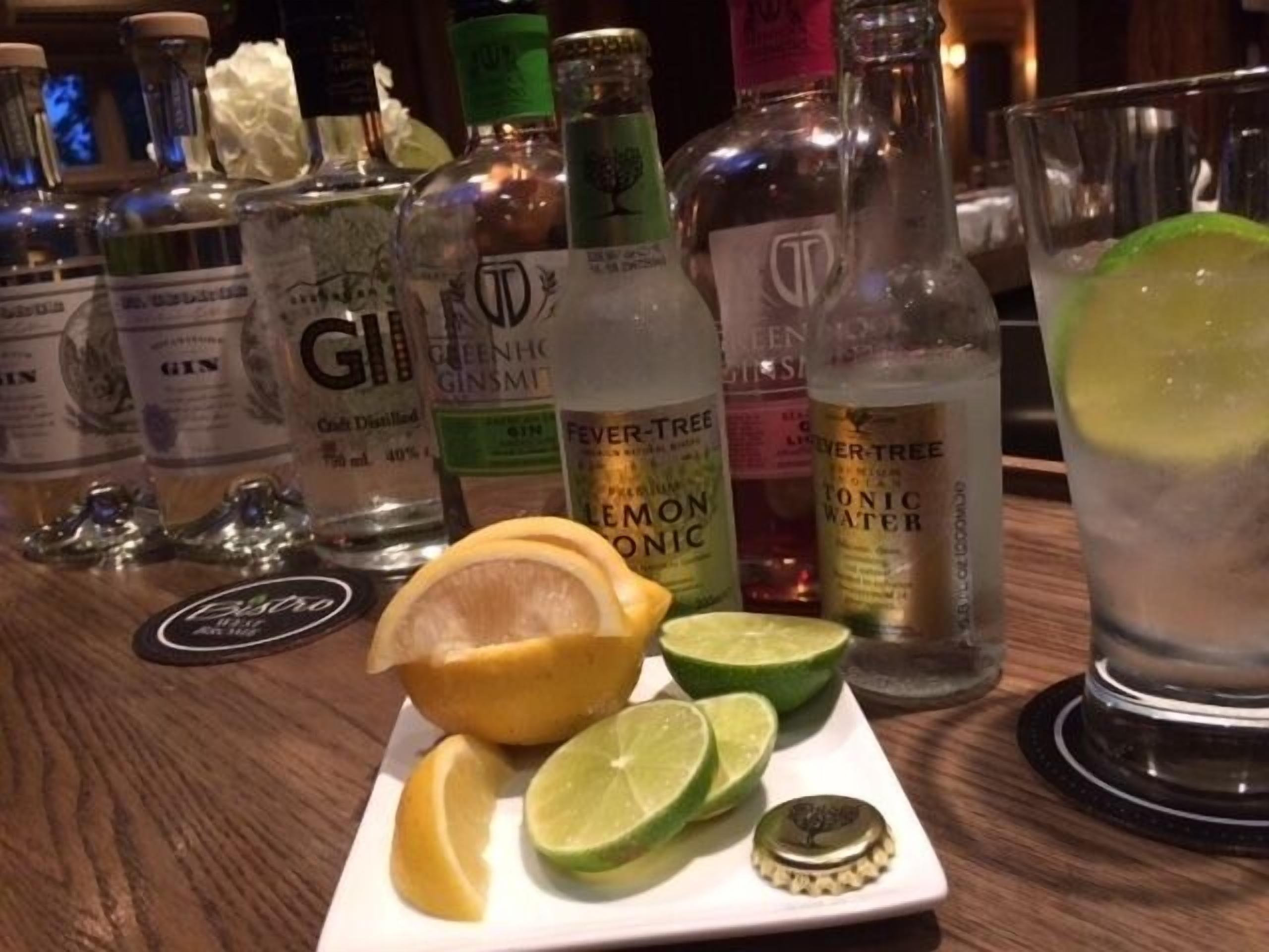 Un bar con diversas botellas de ginebra, tónica de limón y tónica, junto a un vaso con una bebida de lima.