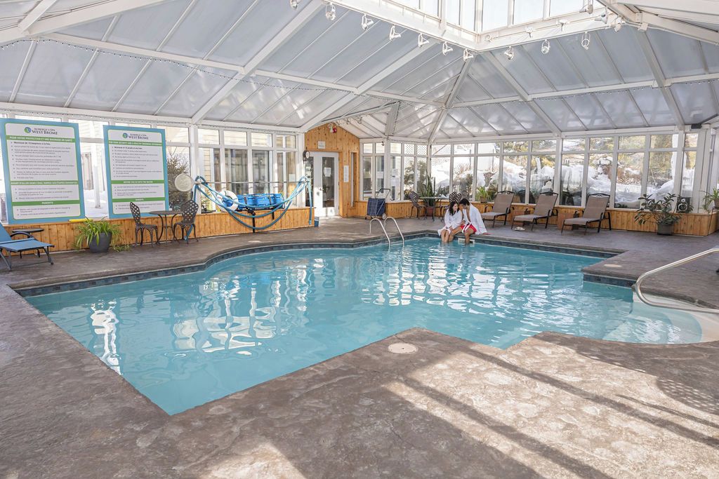 Una piscina interior con techo de vidrio, sillas de descanso y carteles informativos.