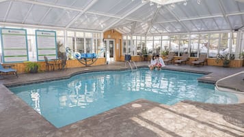 Una piscina interior con techo de vidrio, sillas de descanso y carteles informativos.
