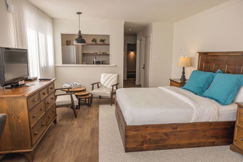 Une chambre d’hôtel avec un lit en bois, un bureau avec une chaise, une télévision et une petite table.