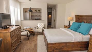 Une chambre d’hôtel avec un lit en bois, un bureau avec une chaise, une télévision et une petite table.