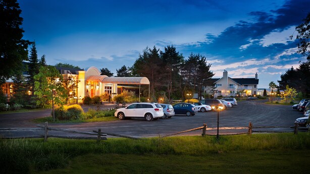 A parking lot with several cars and a building with a covered area. - Auberge West Brome (Lac-Brome)