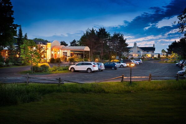 A parking lot with several cars and a building with a covered area. - Auberge West Brome (Lac-Brome)