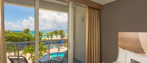 Habitación de hotel con balcón, cama y vistas a una piscina y la playa.