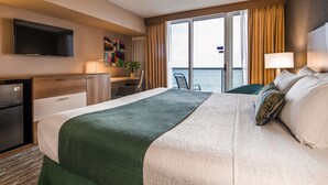 A hotel room with a large bed, a desk, a television, and a view of the sea. - Best Western Plus Atlantic Beach Resort (Miami Beach)