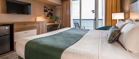 Una habitación de hotel con una cama grande, un escritorio, un televisor y vista al mar.