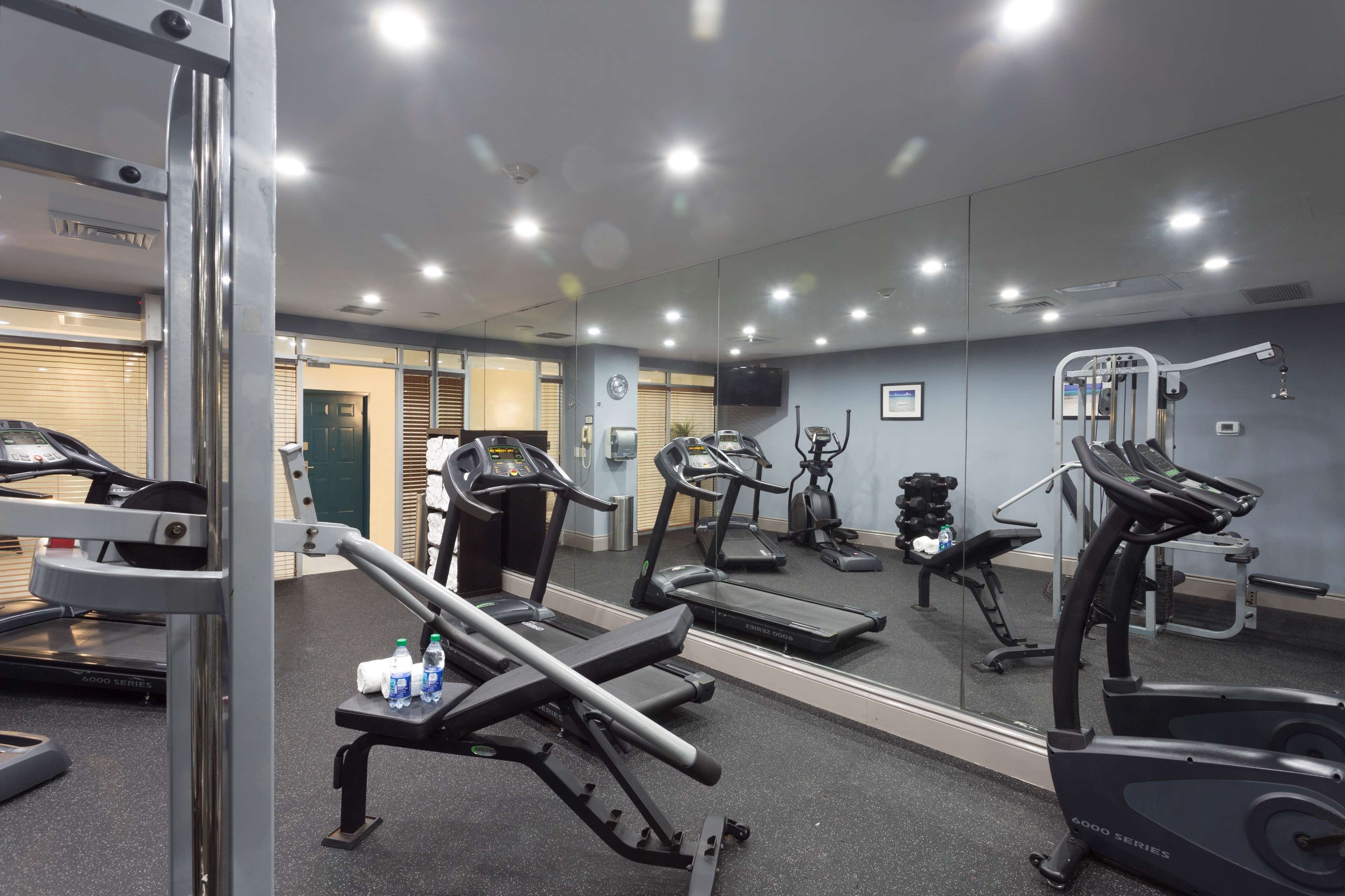 Une salle de sport équipée de matériel d’exercice, d’un tapis de course et d’un mur recouvert de miroirs.