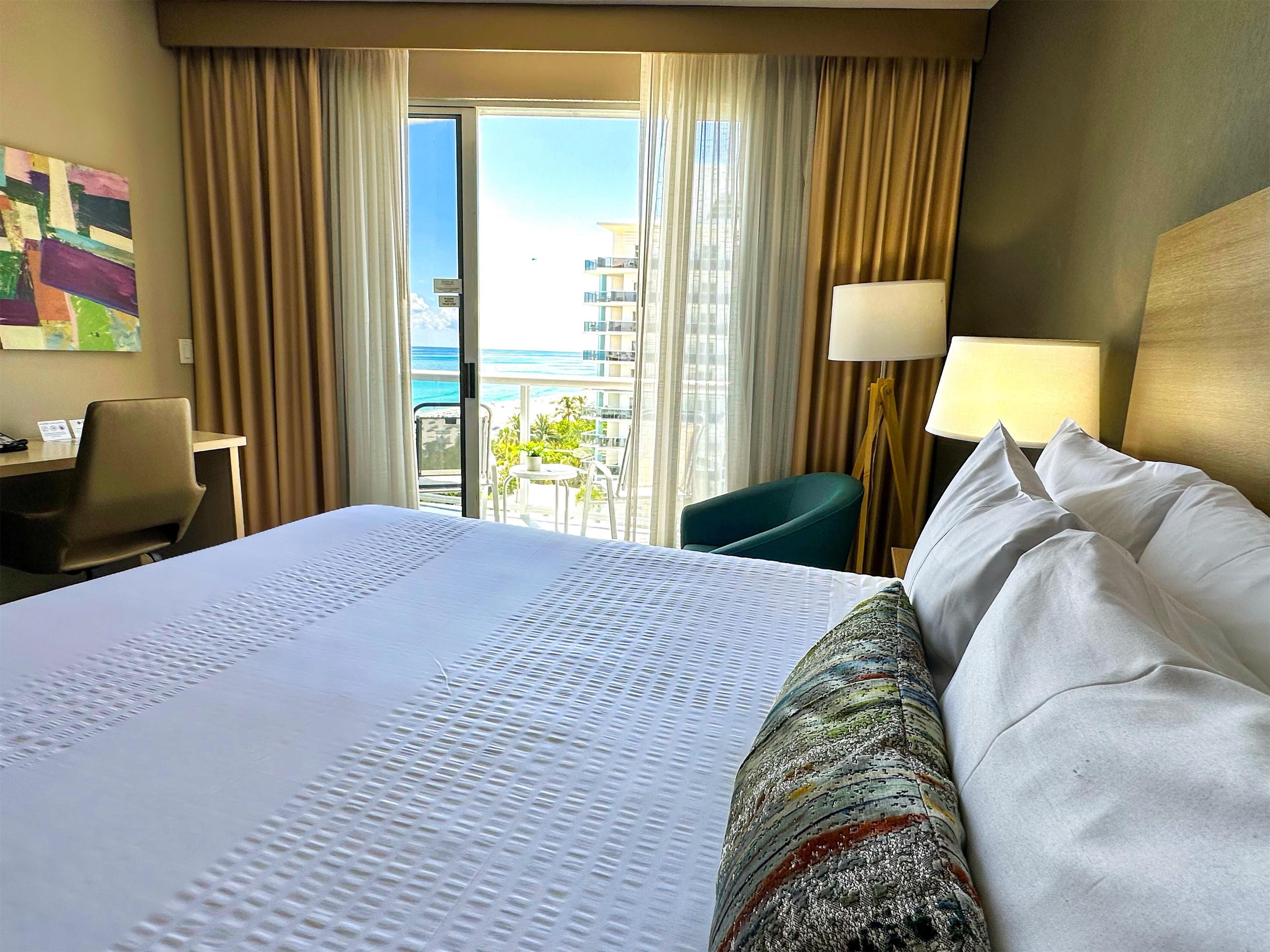 Ein Hotelzimmer mit einem großen Bett, einem Schreibtisch, einem Stuhl und Meerblick aus dem Fenster.