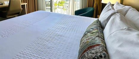 Habitación de hotel con una cama grande, un escritorio, una silla y vista al océano por la ventana.