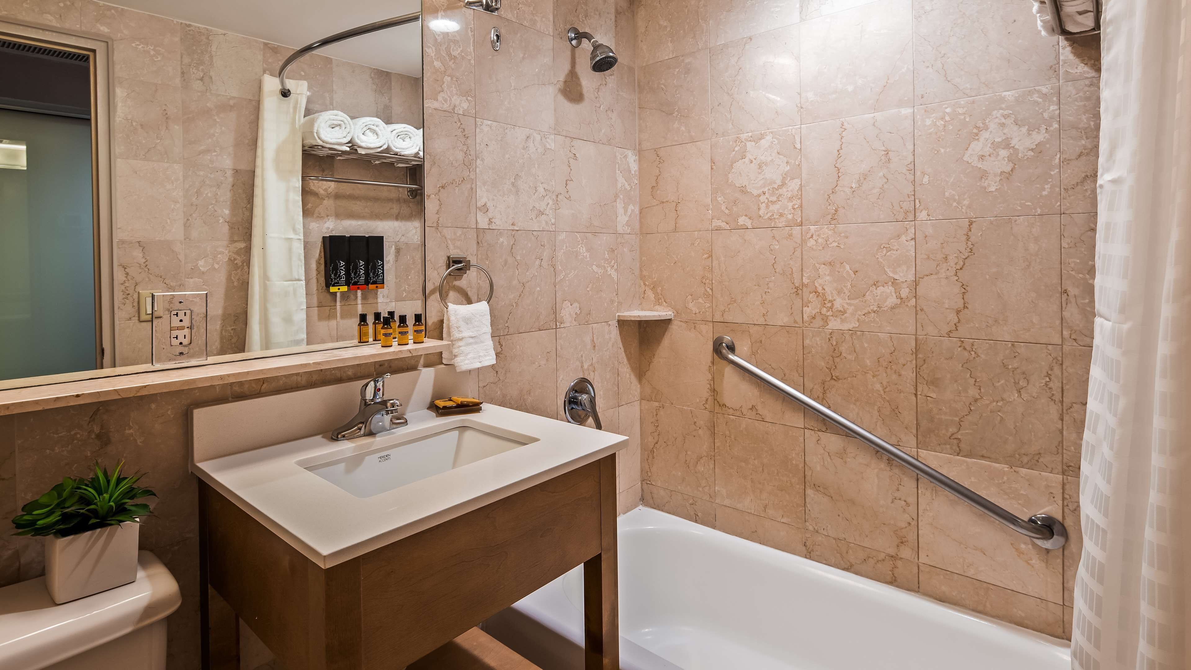 A bathroom with a sink, mirror, shower, and a handrail.