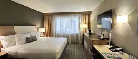 Habitación de hotel con una cama grande, un escritorio con computadora, un televisor y una ventana con cortinas.