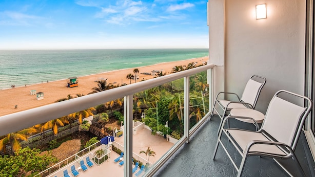 A balcony with a view of a beach, lounge chairs, and a lifeguard tower. - Best Western Plus Atlantic Beach Resort (Miami Beach)