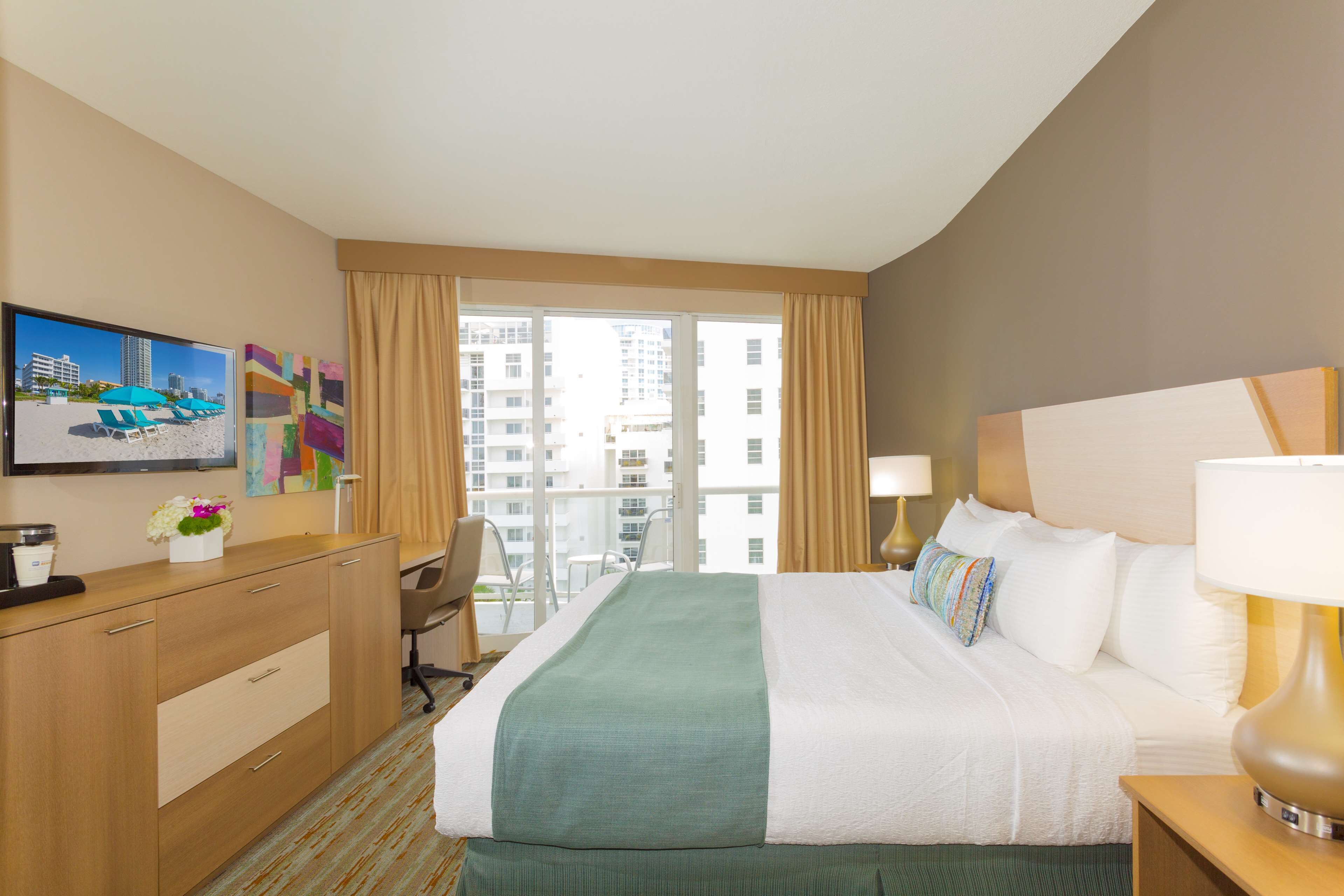 A hotel room with a bed, a desk, a chair, a TV, and a window with curtains.