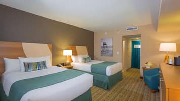 A hotel room with two beds, a desk, a chair, and a door leading to a bathroom.