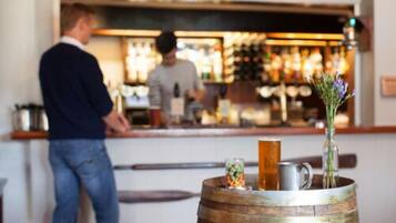 A bar area with a wooden barrel, a glass with a drink, and a vase with flowers.