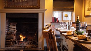 A cozy room with a fireplace, wooden furniture, and a dining table set with plates and glasses. - Master Builders House Hotel (Brockenhurst)