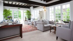 A spacious room with a large window, a sofa, a coffee table, and a desk with a plant. - Master Builders House Hotel (Brockenhurst)