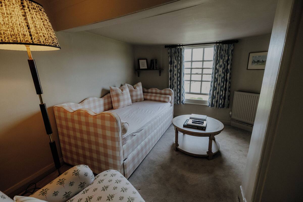 A cozy room with a checkered sofa, a round coffee table, a lamp, and a window with curtains.