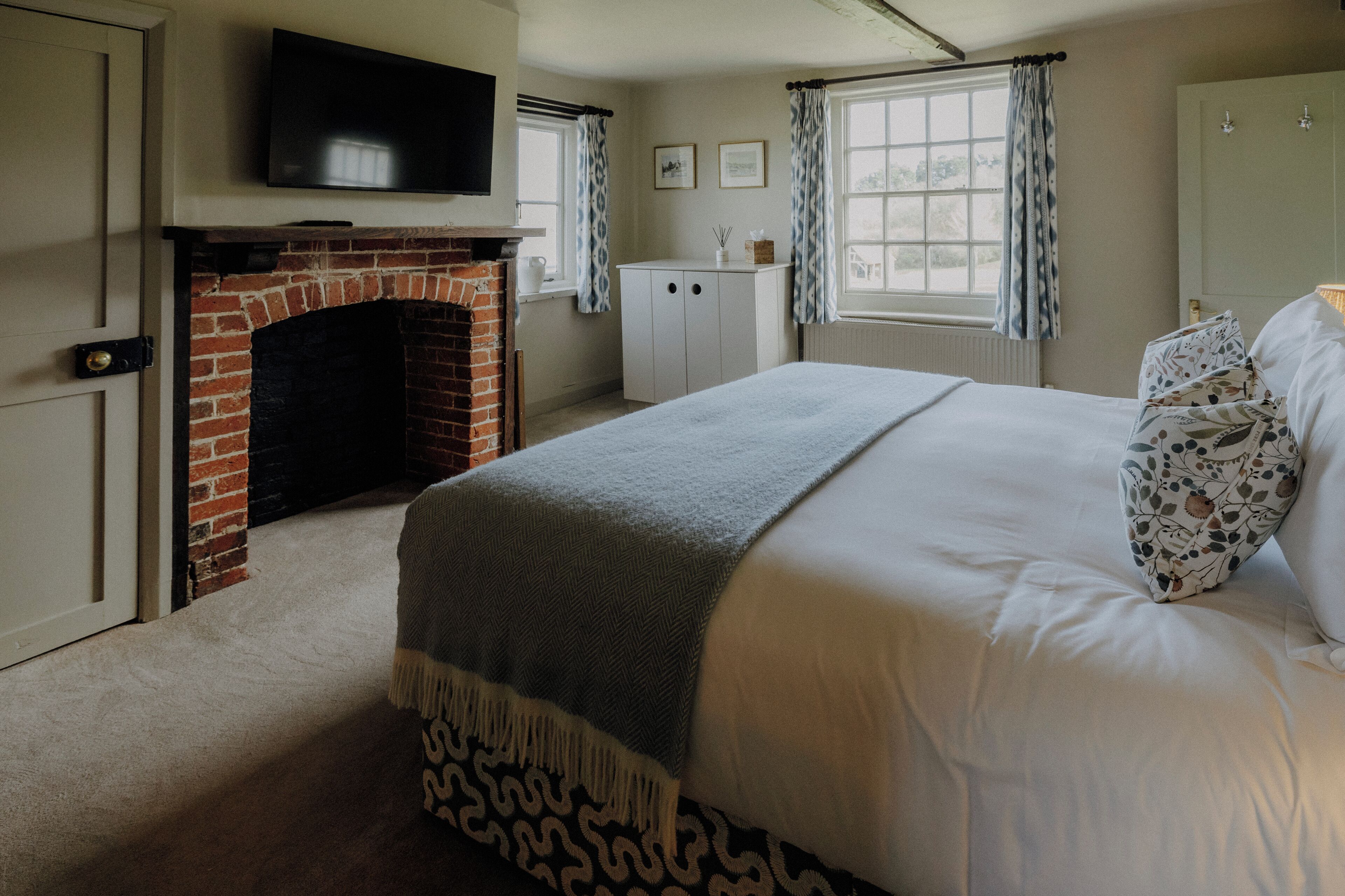 A bedroom with a fireplace, a bed with patterned pillows, a television, and a window with curtains.