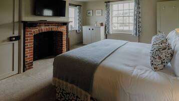 A bedroom with a fireplace, a bed with patterned pillows, a television, and a window with curtains.