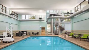 An indoor swimming pool with a central staircase and lounge chairs.