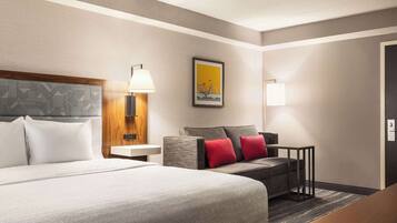 A hotel room with a large bed, a sofa, a small table, and a lamp.