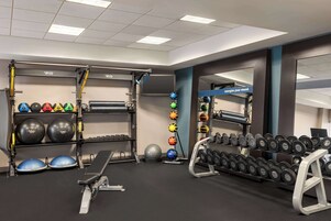 Un gimnasio con equipo de ejercicio, incluyendo mancuernas, balones medicinales y una banca.