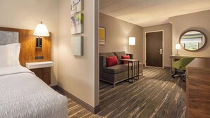 A hotel room with a bed, a desk, a sofa, and a chair. There are wall-mounted lamps and framed pictures. - Hampton Inn by Hilton Shelton (Shelton)