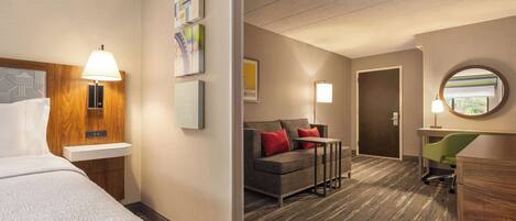 A hotel room with a bed, a desk, a sofa, and a chair. There are wall-mounted lamps and framed pictures.