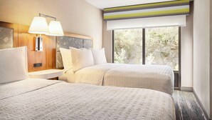 A hotel room with two beds, a nightstand, a lamp, a window with a view of trees, and a ceiling with a light fixture.