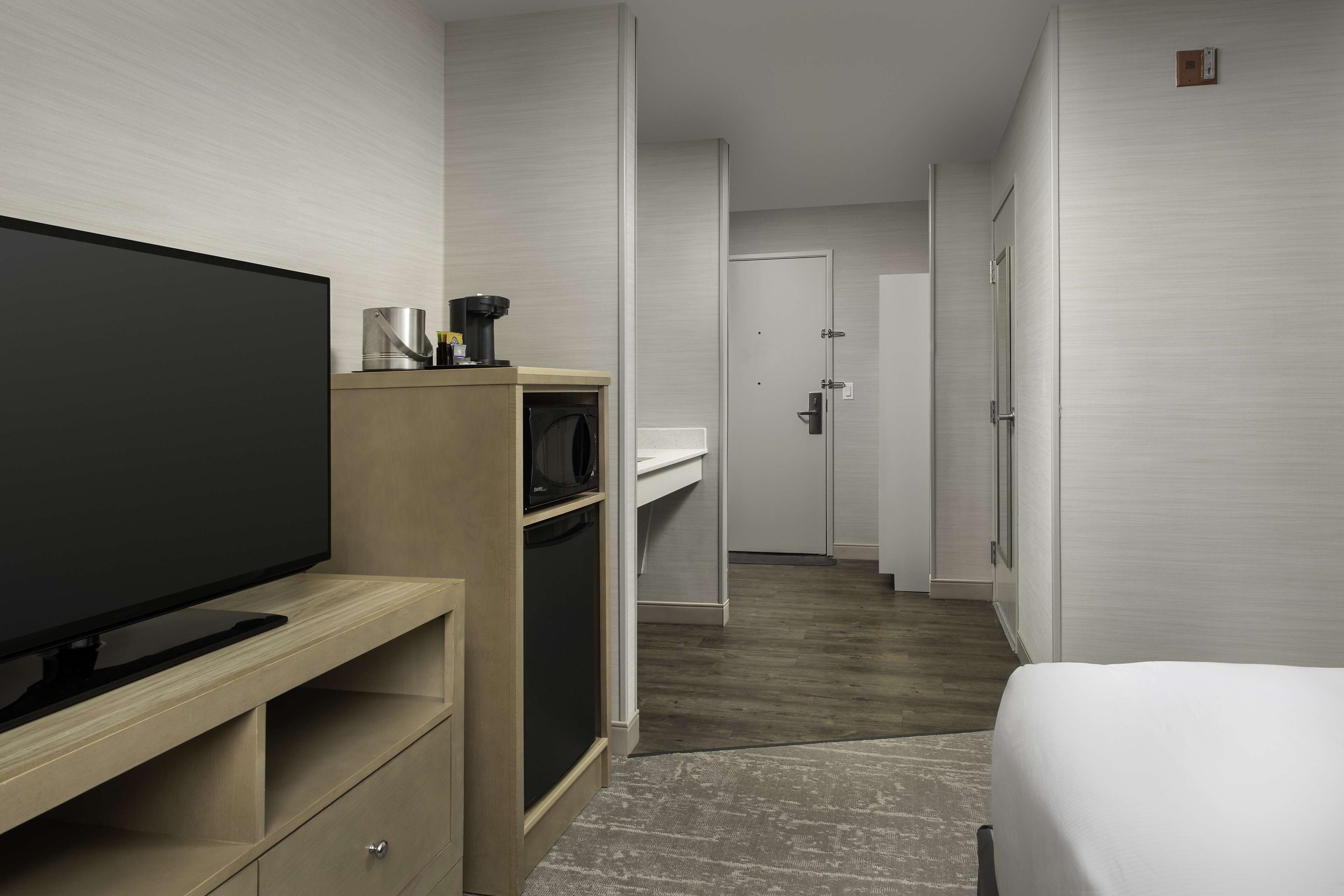 A hotel room with a flat-screen TV, a microwave, a small kitchen area, a bed, and a door leading to another room.