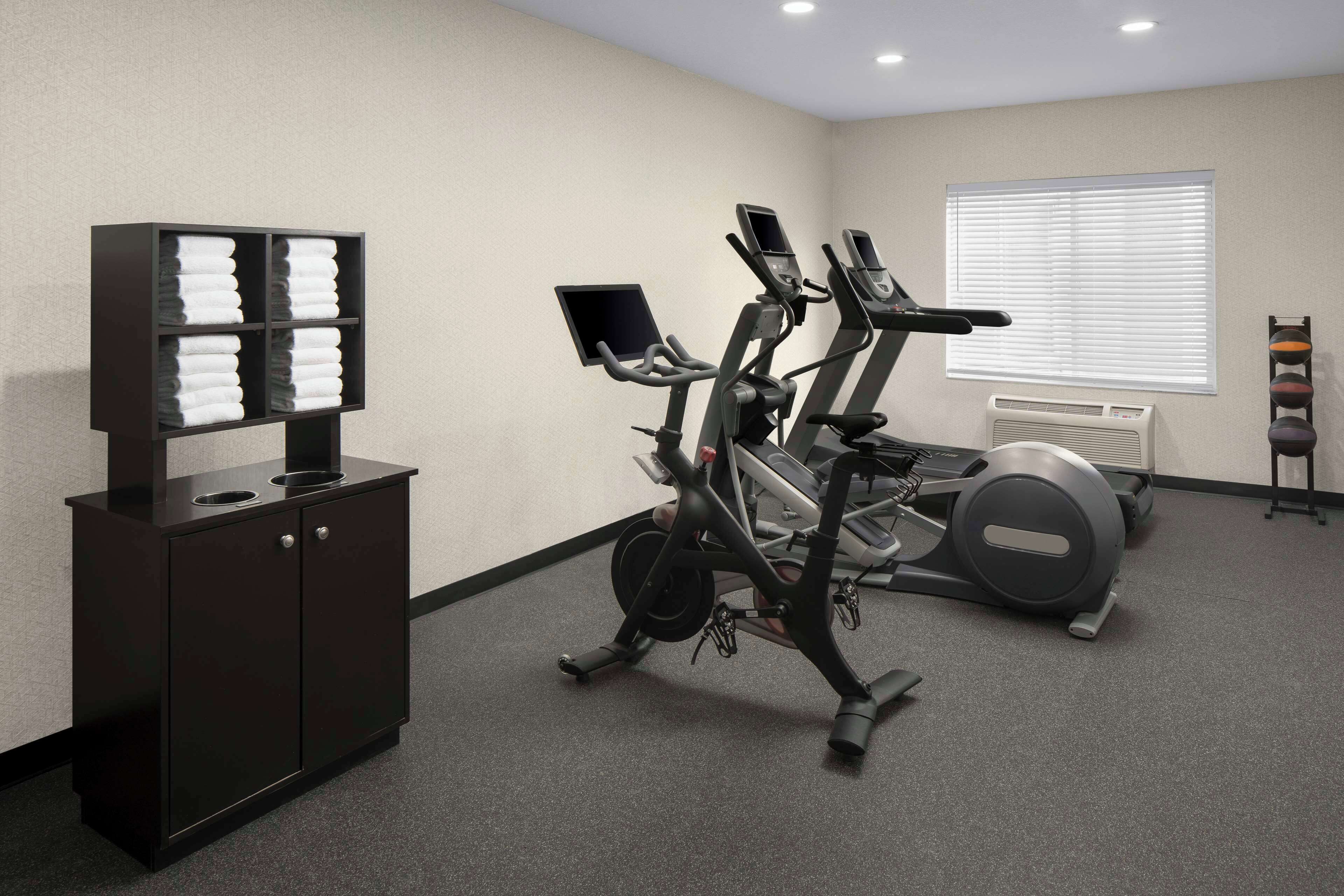 Een fitnessruimte met trainingsapparatuur, een wandairconditioner en een plank met opgevouwen handdoeken.