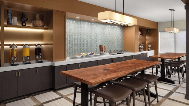A modern kitchen with a wooden dining table, bar stools, and built-in appliances.