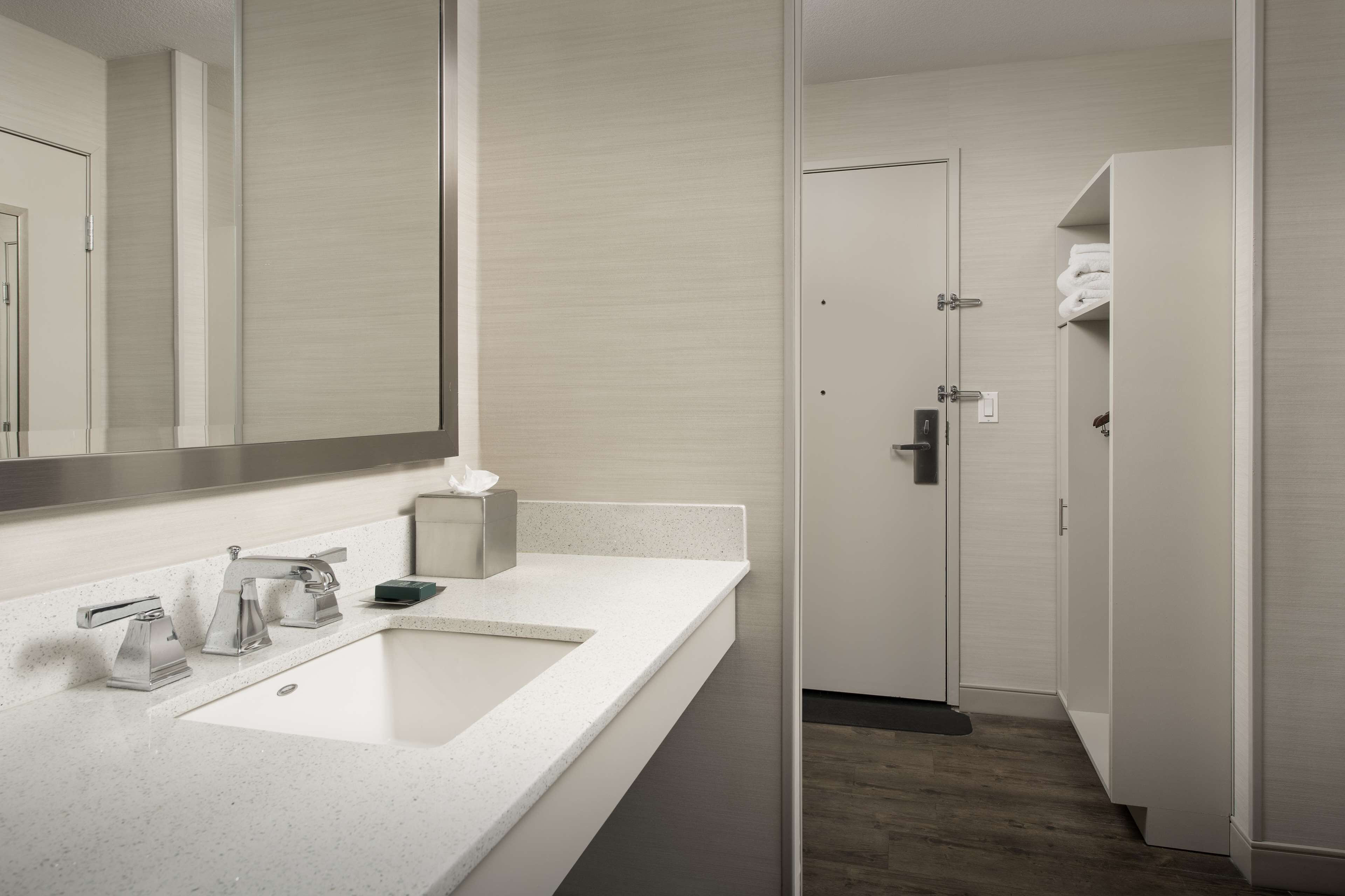A modern bathroom with a large mirror, a white sink, and a door leading to a walk-in closet.