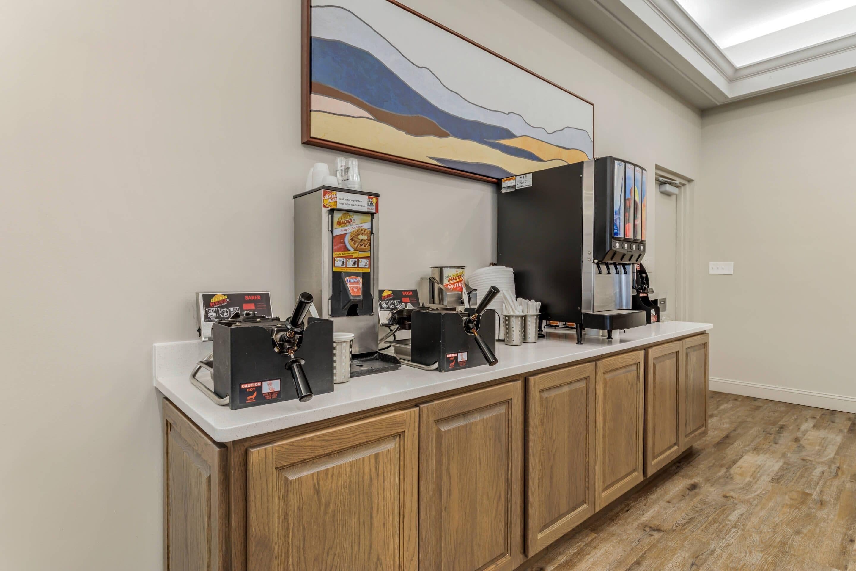Een hotel receptie met een balie, koffieapparaten, een schilderij en een waterkraan.