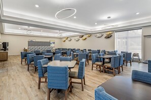 A spacious dining area with multiple tables and chairs, a modern ceiling design, and a large window providing natural light.