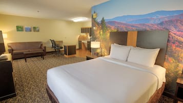 Ett hotellrum med en stor säng, en soffa, ett skrivbord och utsikt över ett bergigt landskap.