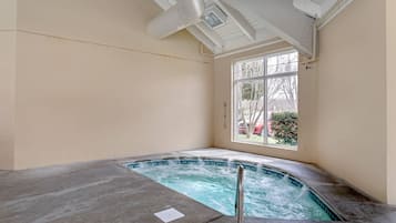 Un jacuzzi en una habitación con un ventanal grande, paredes color beige y un respiradero visible en el techo.