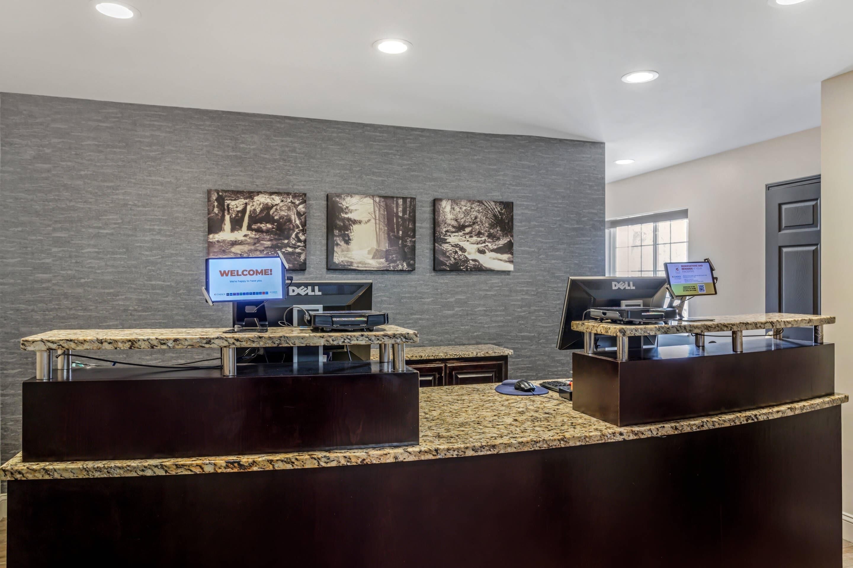 A reception area with a dark wood reception desk, two Dell computers, and a welcome sign.