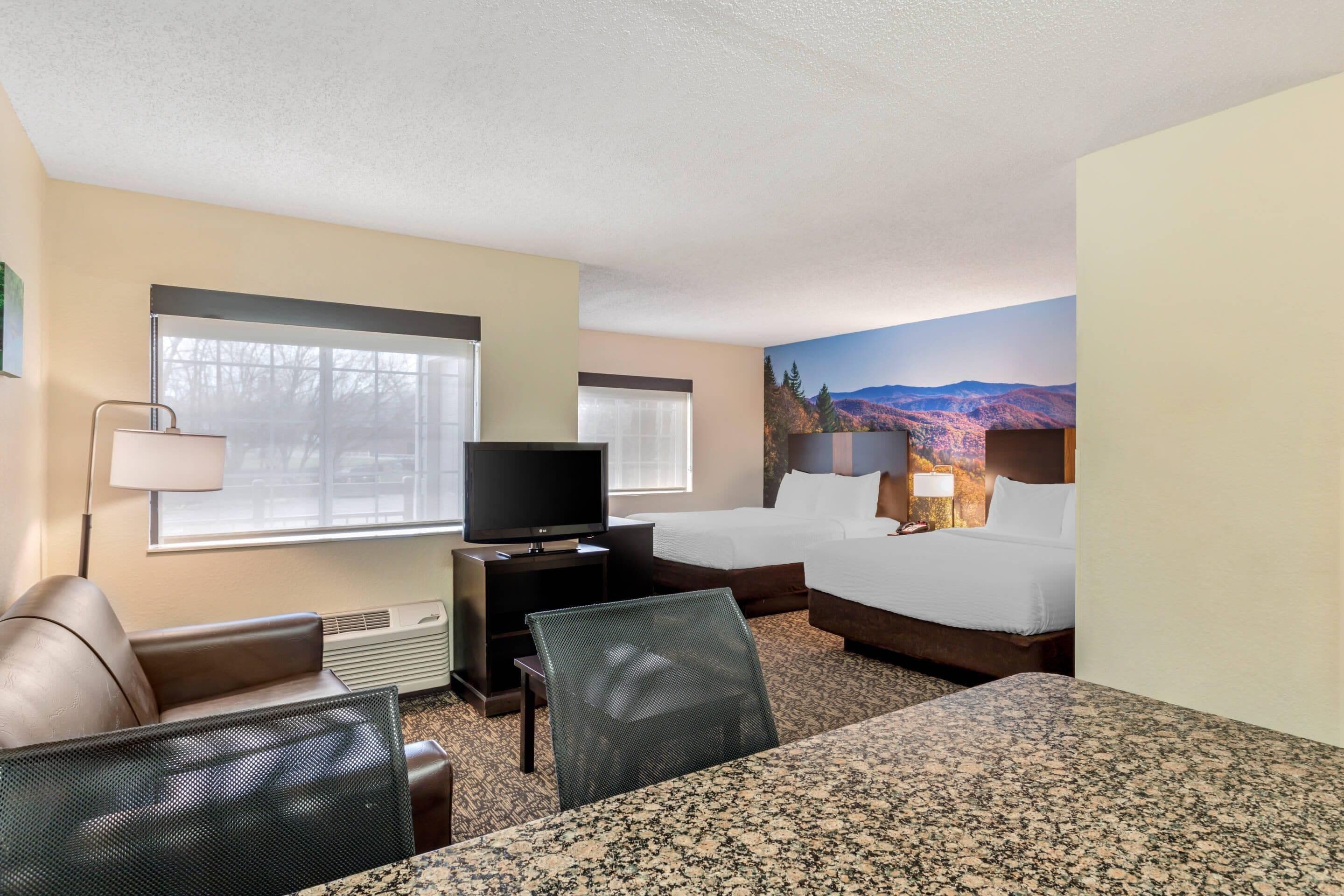 A hotel room with a bed, a desk with a television, a chair, and a large window.