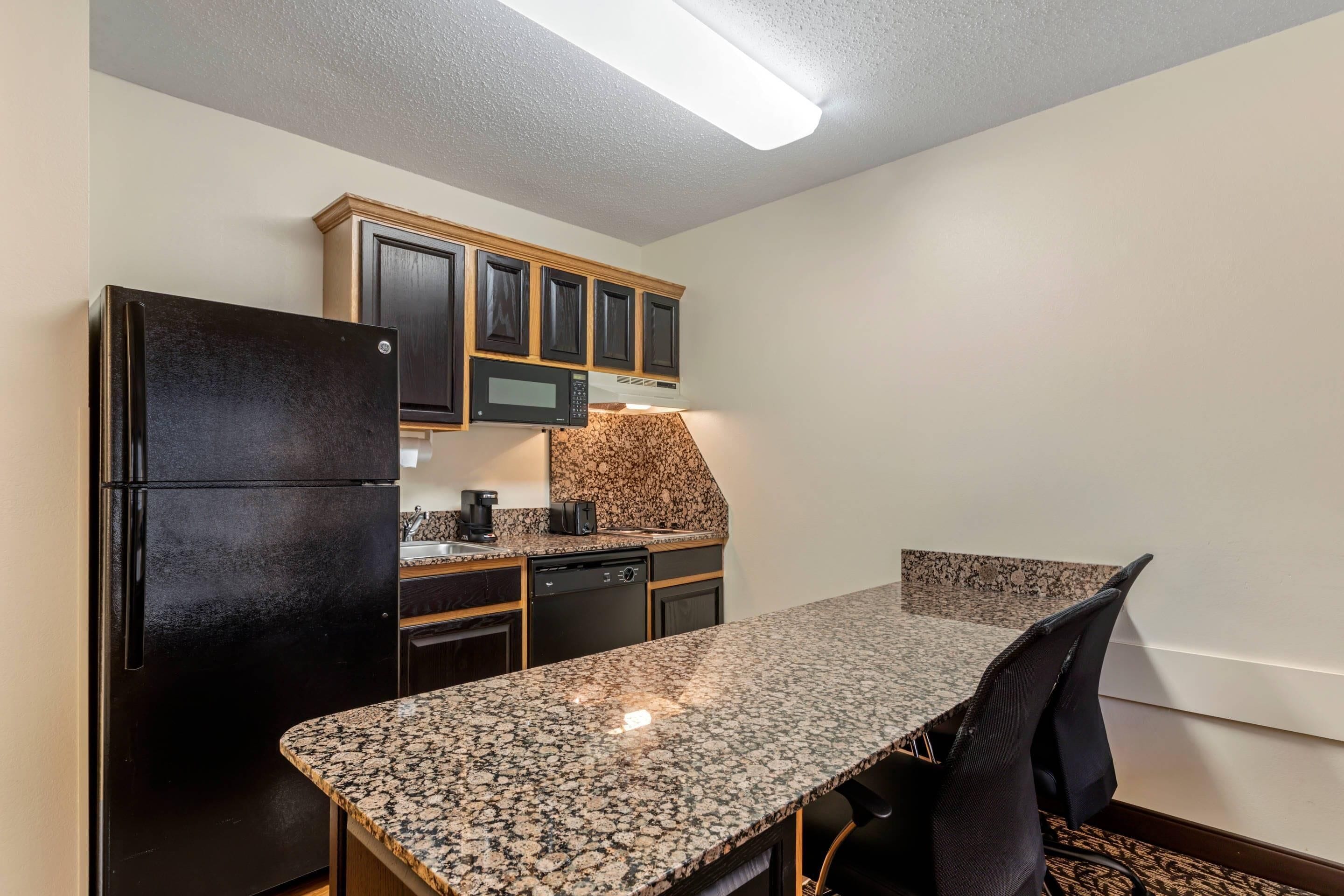 A compact kitchen with a refrigerator, microwave, and built-in oven. There is a dining table with chairs and a granite countertop.