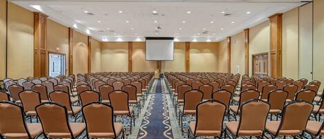 A conference room with rows of chairs, a carpeted floor, and a large screen at the front.