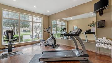 A gym with treadmills, elliptical machines, and weight equipment. Large windows offer views of the outdoors.