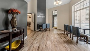 A modern interior with a dark wall, a wooden floor, a vase with flowers, a 'Welcome to Breakfast' sign, and a view through large windows. - LeConte Hotel & Convention Center, an Ascend Collection Hotel (Pigeon Forge)