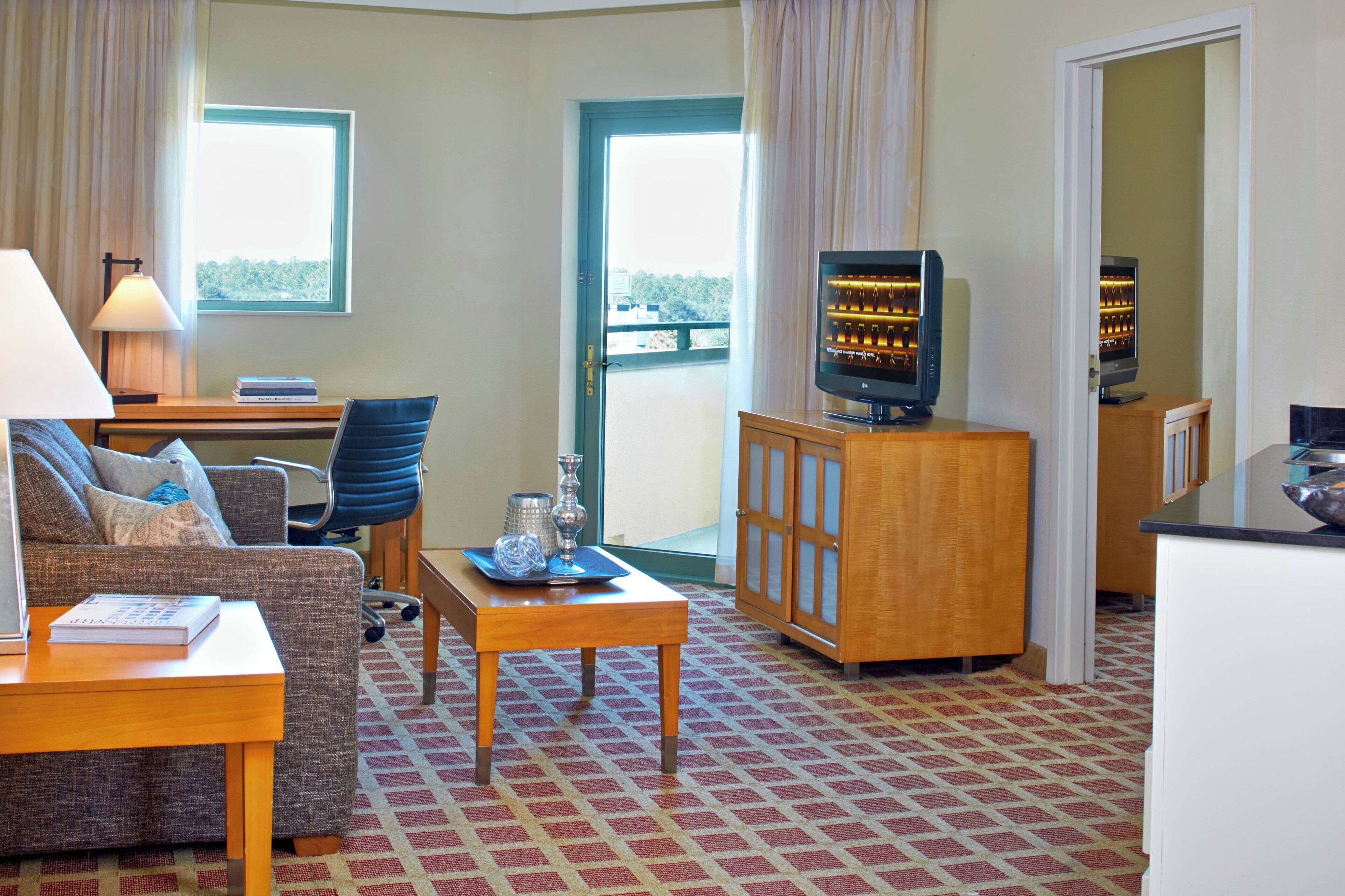 Une chambre d’hôtel avec un canapé, une petite table, un téléviseur posé sur un meuble et une fenêtre avec des rideaux.