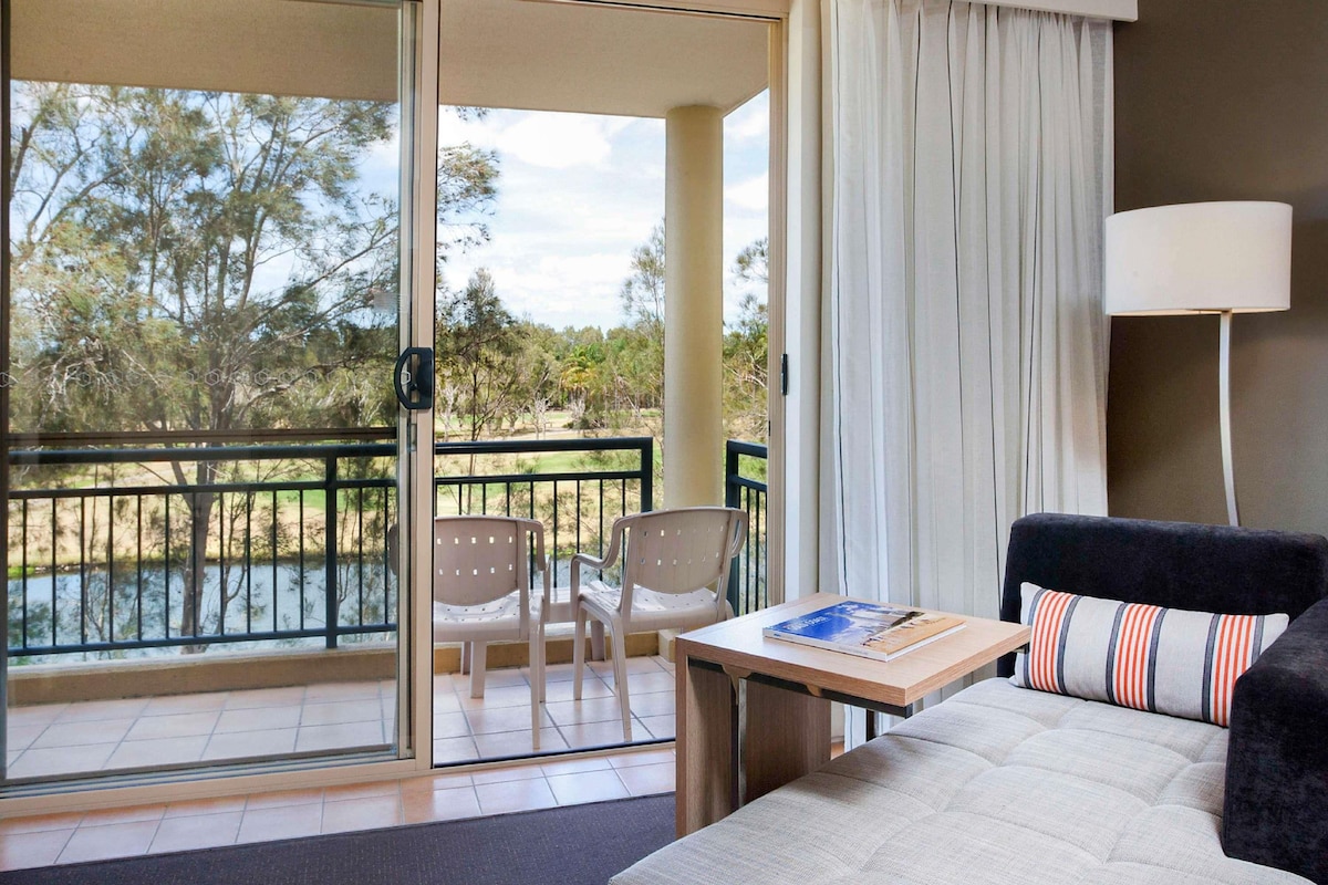 A hotel room with a balcony, a sofa, a small table, and a lamp.